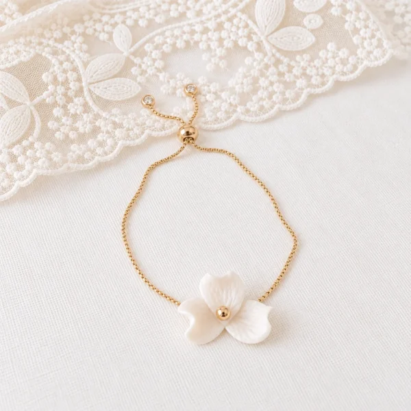 Bracelet NINA posé près d’une dentelle : chaîne dorée réglable, curseur et petits zirconiums aux extrémités, by Marguerite