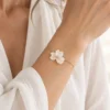 Bracelet NINA porté au poignet avec une chemise blanche en gaze, fleur de porcelaine froide et perle dorée, by Marguerite