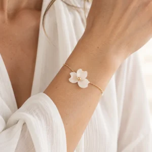 Bracelet NINA porté au poignet avec une chemise blanche en gaze, fleur de porcelaine froide et perle dorée, by Marguerite