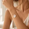 Bracelet de mariage VIVIENNE porté au poignet avec une robe en satin ivoire, pétale nacré sur chaîne dorée, by Marguerite