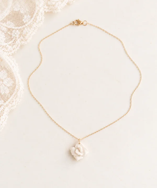 Collier APOLLINE en entier : chaîne fine dorée, fermoir mousqueton et fleur de porcelaine, près d'une dentelle, by Marguerite