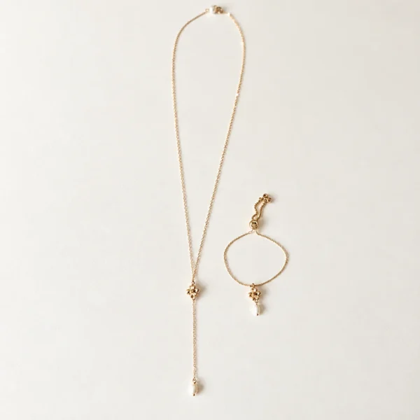 Collier de dos EMMA 8 Une perle ronde à l’avant, et dans le dos une petite fleur dorée suivie d’une perle d’eau douce allongée : EMMA est un collier de dos de mariage à la fleur dorée, fin et lumineux. Sans fermoir, il s’enfile par la tête et dessine une ligne de lumière le long d’une robe dos nu. <ul> <li>Fait main au Pays basque, en France</li> <li>Chaîne gold filled 14 carats, perles d’eau douce, fleur en cuivre doré à l’or fin</li> <li>Longueur 65 ou 70 cm, pendant de 13 cm · longueur personnalisable sur demande</li> </ul> Collier de dos EMMA et bracelet EMMA posés côte à côte : même petite fleur dorée et perles d'eau douce, by Marguerite