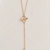 Collier de dos EMMA : petite fleur dorée et perle d'eau douce allongée sur une fine chaîne gold filled, posé sur une toile écrue, by Marguerite
