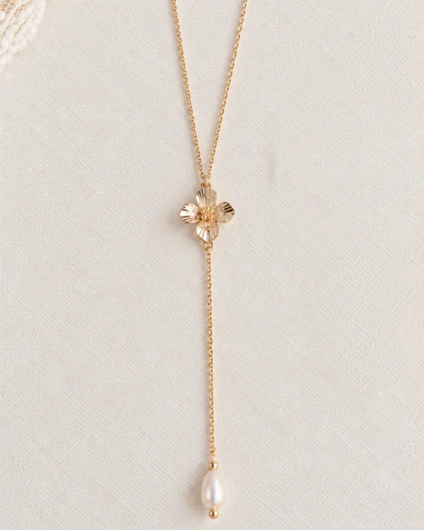 Collier de dos EMMA 9 Une perle ronde à l’avant, et dans le dos une petite fleur dorée suivie d’une perle d’eau douce allongée : EMMA est un collier de dos de mariage à la fleur dorée, fin et lumineux. Sans fermoir, il s’enfile par la tête et dessine une ligne de lumière le long d’une robe dos nu. <ul> <li>Fait main au Pays basque, en France</li> <li>Chaîne gold filled 14 carats, perles d’eau douce, fleur en cuivre doré à l’or fin</li> <li>Longueur 65 ou 70 cm, pendant de 13 cm · longueur personnalisable sur demande</li> </ul> Collier de dos EMMA : petite fleur dorée et perle d'eau douce allongée sur une fine chaîne gold filled, posé sur une toile écrue, by Marguerite