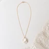 Collier de mariage GARANCE : pétales de porcelaine froide blanche texturés et superposés sur chaîne gold filled, posé près d’une dentelle, by Marguerite