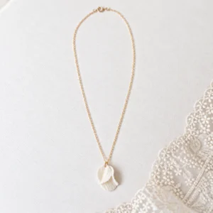 Collier de mariage GARANCE : pétales de porcelaine froide blanche texturés et superposés sur chaîne gold filled, posé près d’une dentelle, by Marguerite