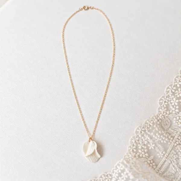 Collier GARANCE 5 Deux pétales de porcelaine froide blanche, creusés de fines stries et posés l’un sur l’autre au bout d’une chaîne fine : GARANCE est un collier pétales délicat, qui reprend la matière de toute la ligne GARANCE. Il se porte le jour J, puis tous les jours. <ul> <li>Fait main au Pays basque, en France</li> <li>Deux pétales texturés en porcelaine froide, le plus grand d’environ 2 cm, chaîne en gold filled 14k</li> <li>Longueur au choix : 42, 45 ou 48 cm</li> </ul> Collier de mariage GARANCE : pétales de porcelaine froide blanche texturés et superposés sur chaîne gold filled, posé près d’une dentelle, by Marguerite