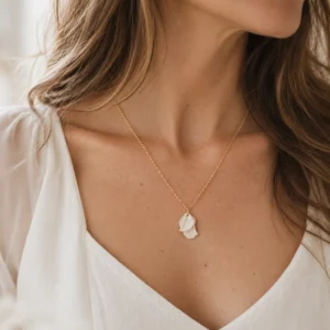 Collier GARANCE porté avec une robe blanche à décolleté en V : petit pendentif de pétales texturés en porcelaine sur chaîne dorée, by Marguerite