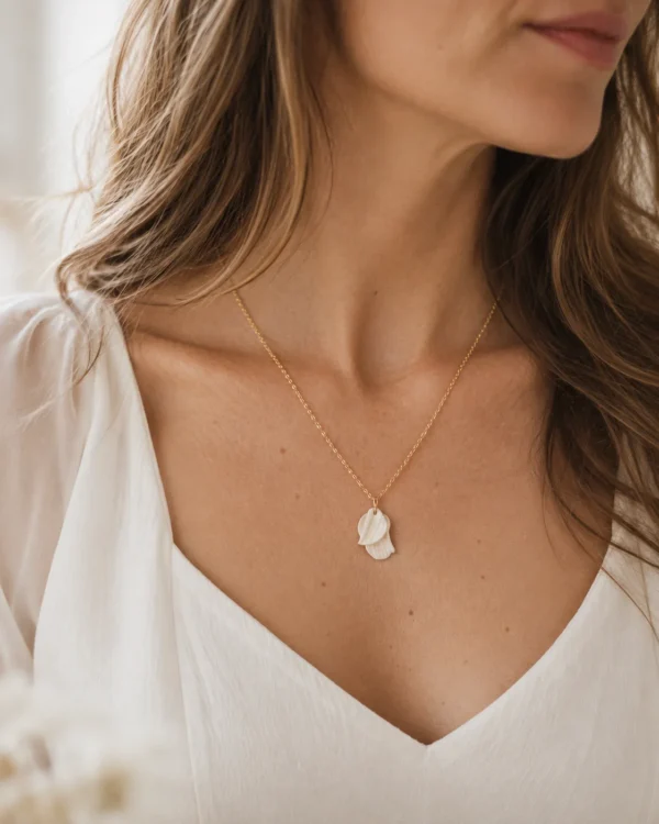 Collier GARANCE 6 Deux pétales de porcelaine froide blanche, creusés de fines stries et posés l’un sur l’autre au bout d’une chaîne fine : GARANCE est un collier pétales délicat, qui reprend la matière de toute la ligne GARANCE. Il se porte le jour J, puis tous les jours. <ul> <li>Fait main au Pays basque, en France</li> <li>Deux pétales texturés en porcelaine froide, le plus grand d’environ 2 cm, chaîne en gold filled 14k</li> <li>Longueur au choix : 42, 45 ou 48 cm</li> </ul> Collier GARANCE porté avec une robe blanche à décolleté en V : petit pendentif de pétales texturés en porcelaine sur chaîne dorée, by Marguerite
