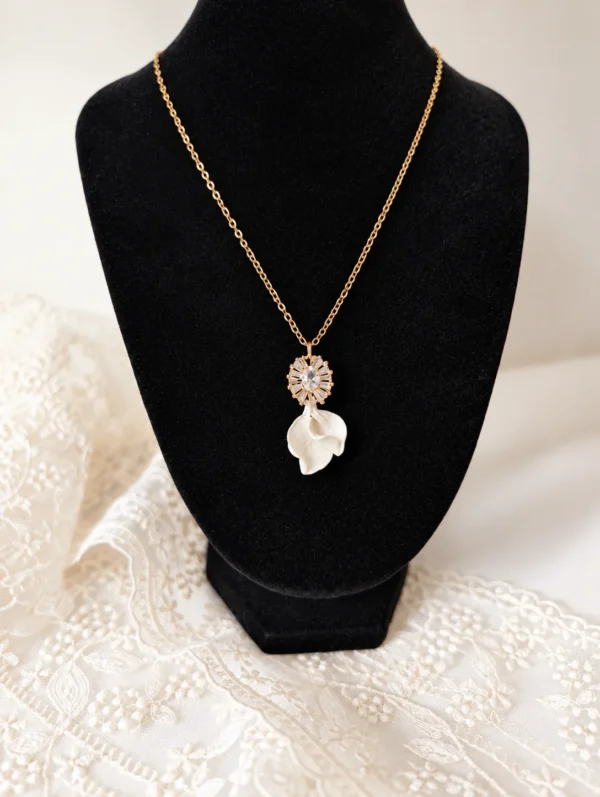 Collier STELLA 11 Deux petits pétales de porcelaine froide blanche, posés l’un sur l’autre sous un pendentif serti de zircones : STELLA est un collier de mariée lumineux, assorti aux boucles d’oreilles STELLA. Il brille le jour J, puis se porte au quotidien. <ul> <li>Fait main au Pays basque, en France</li> <li>Pendentif d’environ 2,5 cm : zircones cubiques et pétales en porcelaine froide</li> <li>Chaîne gold filled 14 carats, 42, 45 ou 48 cm</li> </ul> Collier STELLA sur un buste noir : fine chaîne gold filled, pendentif serti et pétales de porcelaine blanche, by Marguerite