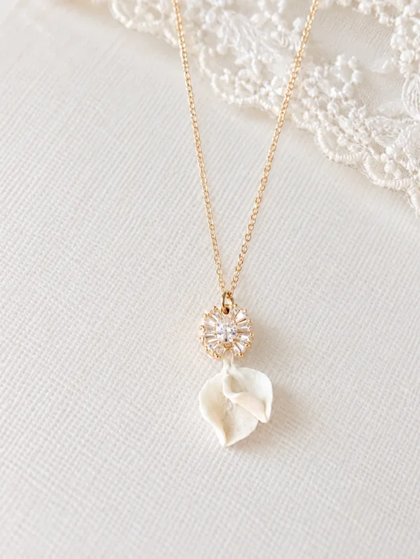 Collier STELLA 9 Deux petits pétales de porcelaine froide blanche, posés l’un sur l’autre sous un pendentif serti de zircones : STELLA est un collier de mariée lumineux, assorti aux boucles d’oreilles STELLA. Il brille le jour J, puis se porte au quotidien. <ul> <li>Fait main au Pays basque, en France</li> <li>Pendentif d’environ 2,5 cm : zircones cubiques et pétales en porcelaine froide</li> <li>Chaîne gold filled 14 carats, 42, 45 ou 48 cm</li> </ul> Collier de mariée STELLA : pendentif serti de zircones et deux pétales de porcelaine froide blanche sur chaîne gold filled, by Marguerite