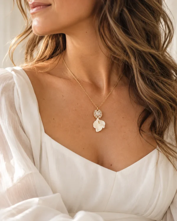 Collier STELLA 10 Deux petits pétales de porcelaine froide blanche, posés l’un sur l’autre sous un pendentif serti de zircones : STELLA est un collier de mariée lumineux, assorti aux boucles d’oreilles STELLA. Il brille le jour J, puis se porte au quotidien. <ul> <li>Fait main au Pays basque, en France</li> <li>Pendentif d’environ 2,5 cm : zircones cubiques et pétales en porcelaine froide</li> <li>Chaîne gold filled 14 carats, 42, 45 ou 48 cm</li> </ul> Collier STELLA porté avec un décolleté en V blanc : pendentif zircones et pétales de porcelaine au creux du cou, by Marguerite