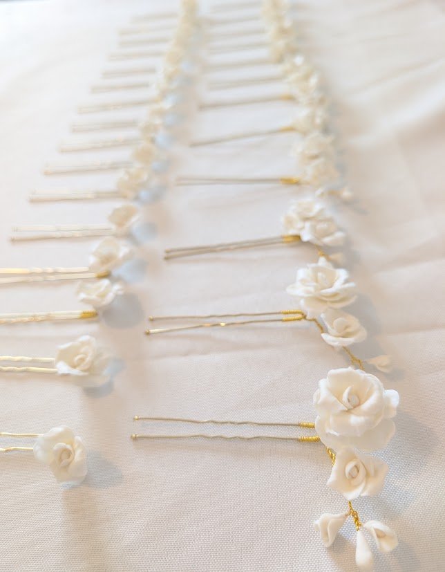 Ma façon de créer : en petite série, pétale après pétale 1 Épingles à cheveux de mariée alignées sur la table de l'atelier, roses de porcelaine froide blanche sur tiges dorées, préparées en petite série, by Marguerite