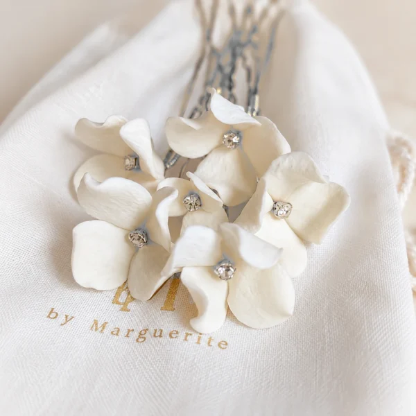 Épingles PAULINE 6 <p>Une petite fleur de porcelaine froide à peine éclose par épingle, chacune différente, de 1,5 à 3 cm, autour d’un strass : PAULINE, ce sont des épingles à chignon de mariée que vous choisissez à l’unité, de deux à sept. Je compose l’assortiment en mêlant les tailles, pour que les fleurs s’accordent comme un petit bouquet dans votre coiffure.</p><ul><li>Fait main au Pays basque, en France</li><li>Fleurs en porcelaine froide, cœur en strass, épingles en U de 7 cm</li><li>De 2 à 7 épingles · version dorée ou argentée</li></ul> Épingles PAULINE argentées : fleurs de porcelaine froide blanche, strass et épingles en U argentées, by Marguerite