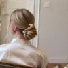 Coiffure de mariée vue de dos, chignon bas torsadé avec deux fleurs PAULINE pendant les préparatifs, by Marguerite