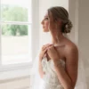 Mariée de profil près d’une fenêtre, chignon bas fleuri d’une épingle PAULINE et voile de tulle, by Marguerite