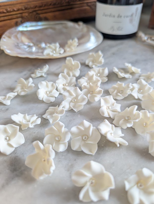 Ma façon de créer : en petite série, pétale après pétale 2 Fleurs de porcelaine froide blanche au cœur de perle, façonnées une à une et posées sur le marbre de l'atelier avant montage, by Marguerite