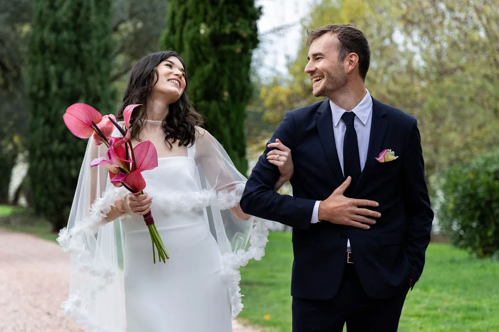 Couple de mariés dans un parc, la mariée en cape de tulle avec un bouquet d'anthuriums, by Marguerite