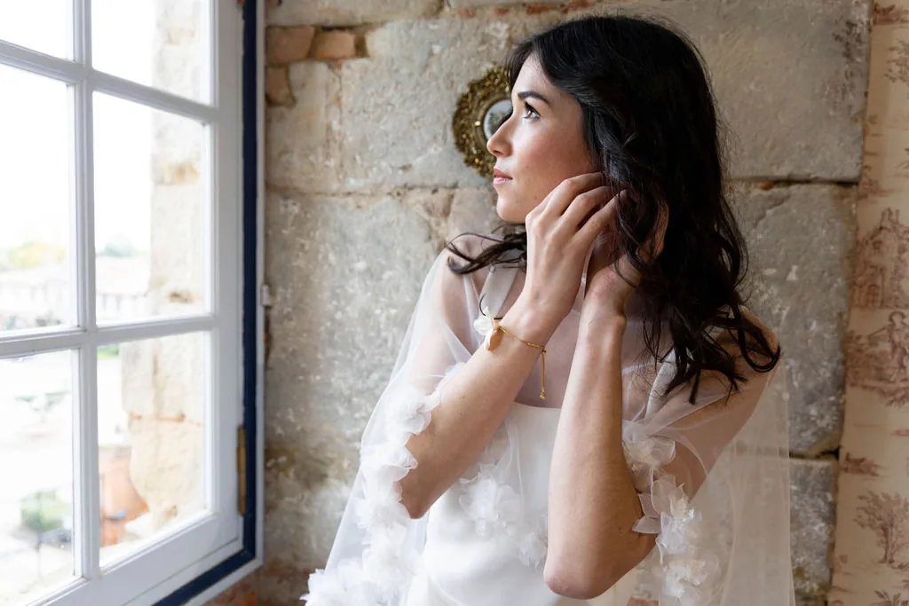 Accueil 18 Mariée en cape de tulle fleurie près d'une fenêtre, bracelet GARANCE au poignet, by Marguerite