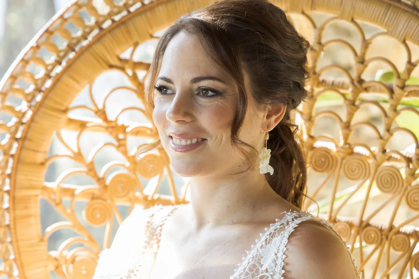 Mariée souriante dans un fauteuil en rotin avec les boucles d'oreilles HÉLÈNE en porcelaine froide, by Marguerite