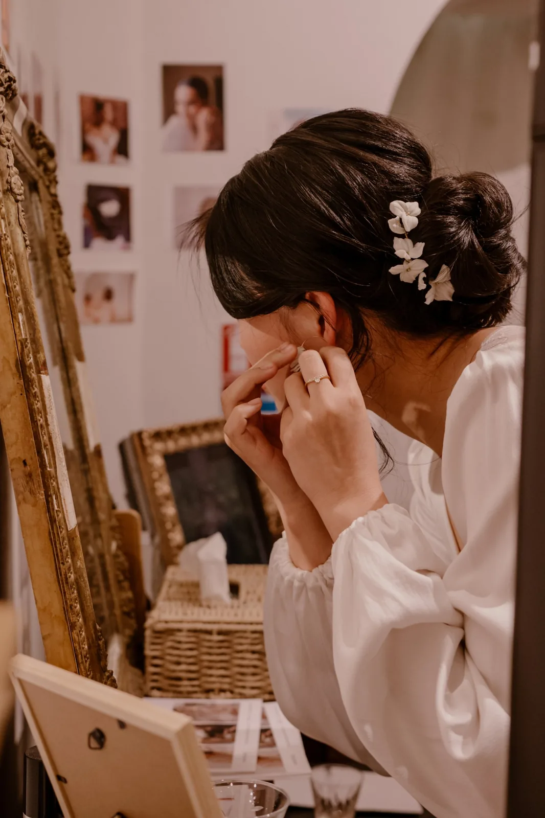 Où trouver mes créations 1 Mariée essayant des boucles d'oreilles devant un miroir doré, peigne de fleurs en porcelaine froide dans le chignon, by Marguerite