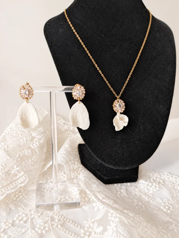 Collier STELLA 12 Deux petits pétales de porcelaine froide blanche, posés l’un sur l’autre sous un pendentif serti de zircones : STELLA est un collier de mariée lumineux, assorti aux boucles d’oreilles STELLA. Il brille le jour J, puis se porte au quotidien. <ul> <li>Fait main au Pays basque, en France</li> <li>Pendentif d’environ 2,5 cm : zircones cubiques et pétales en porcelaine froide</li> <li>Chaîne gold filled 14 carats, 42, 45 ou 48 cm</li> </ul> Parure de mariée STELLA : collier et boucles d’oreilles assortis, zircones et pétales de porcelaine froide blanche, by Marguerite